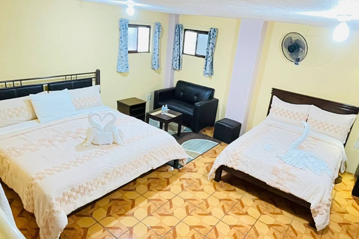Une chambre d’hôtel avec deux lits, un canapé, une petite table et un ventilateur.