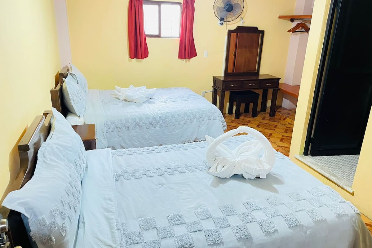 Une chambre avec deux lits, un bureau, une chaise, un ventilateur et une armoire.
