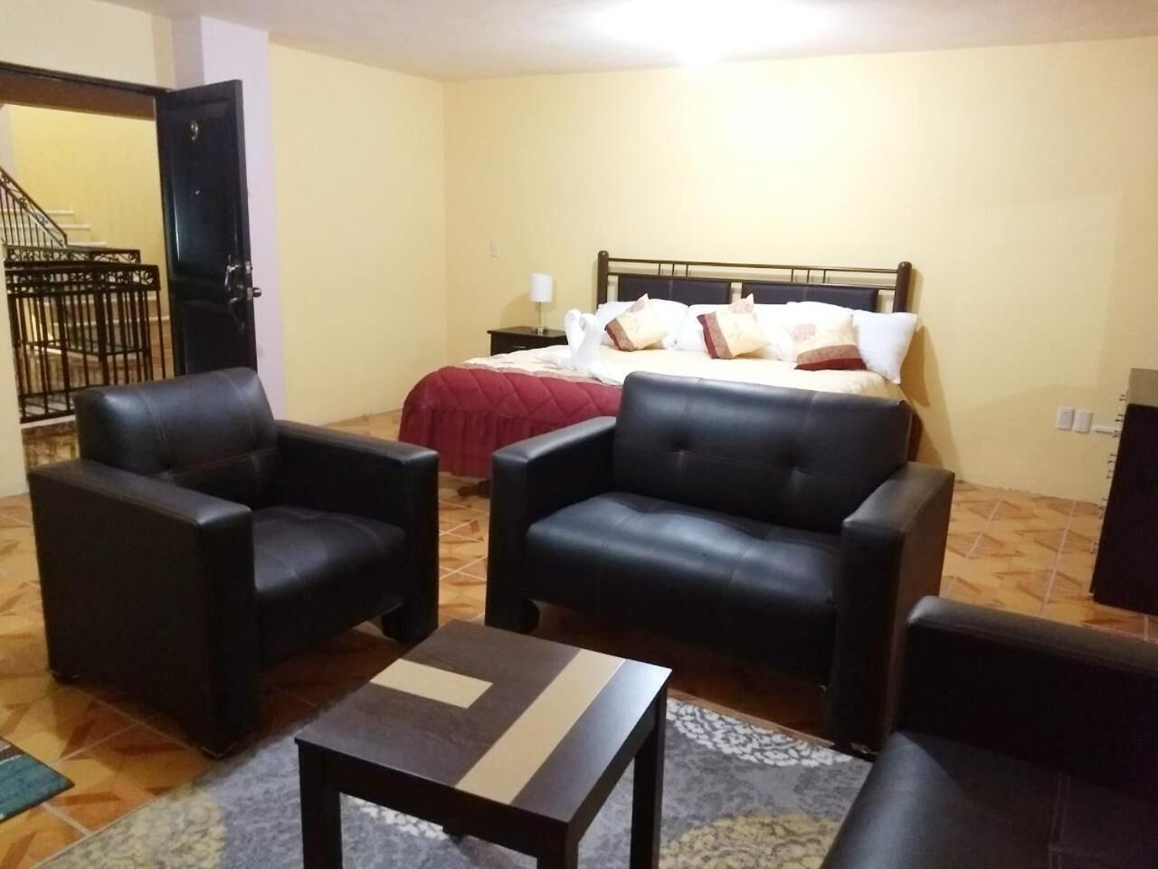 Een hotelkamer met een bed, twee zwarte leren fauteuils, een tafeltje en een nachtkastje met een lamp.
