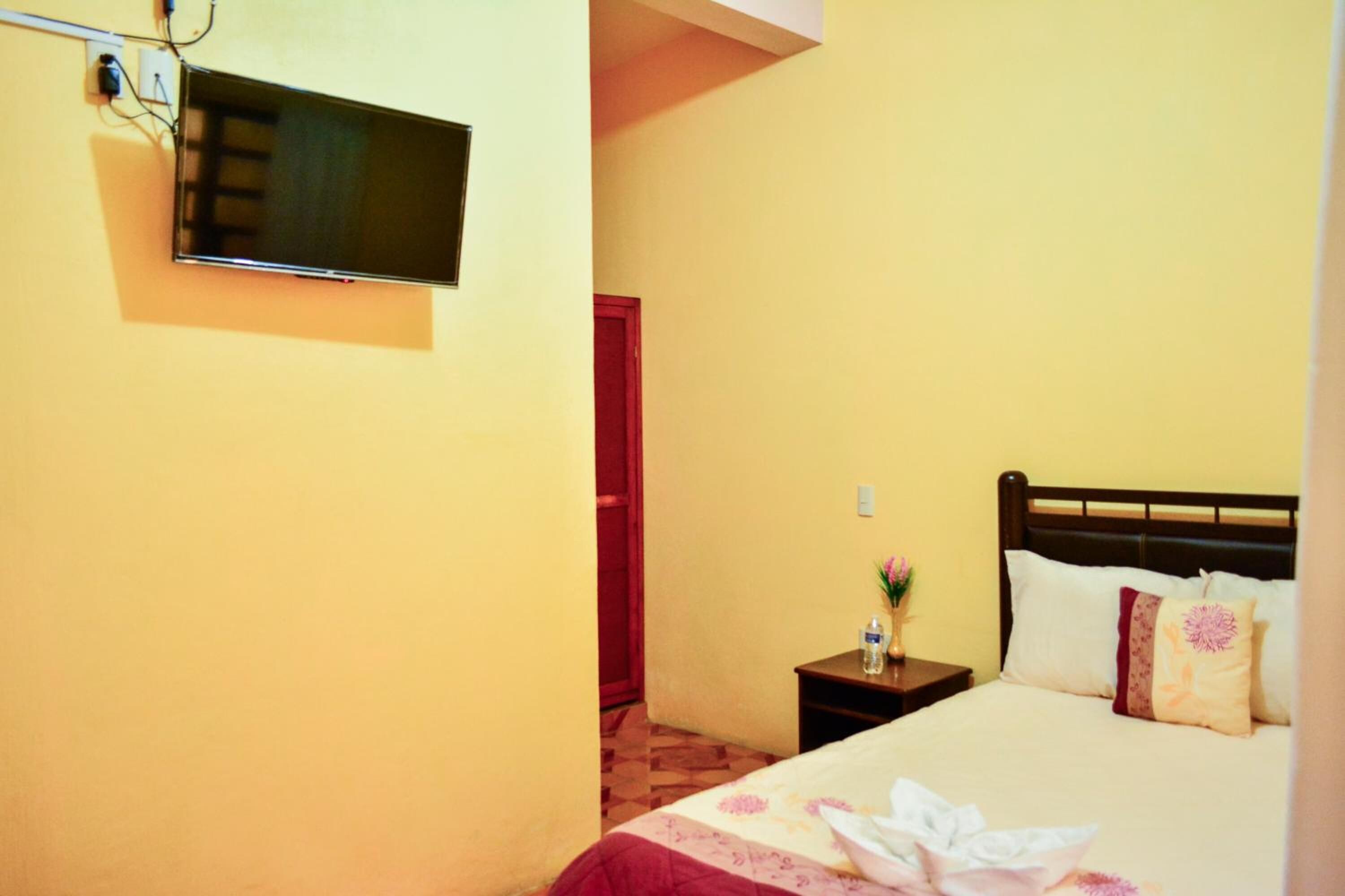 A hotel room with a bed, a bedside table with a vase, and a TV mounted on the wall.