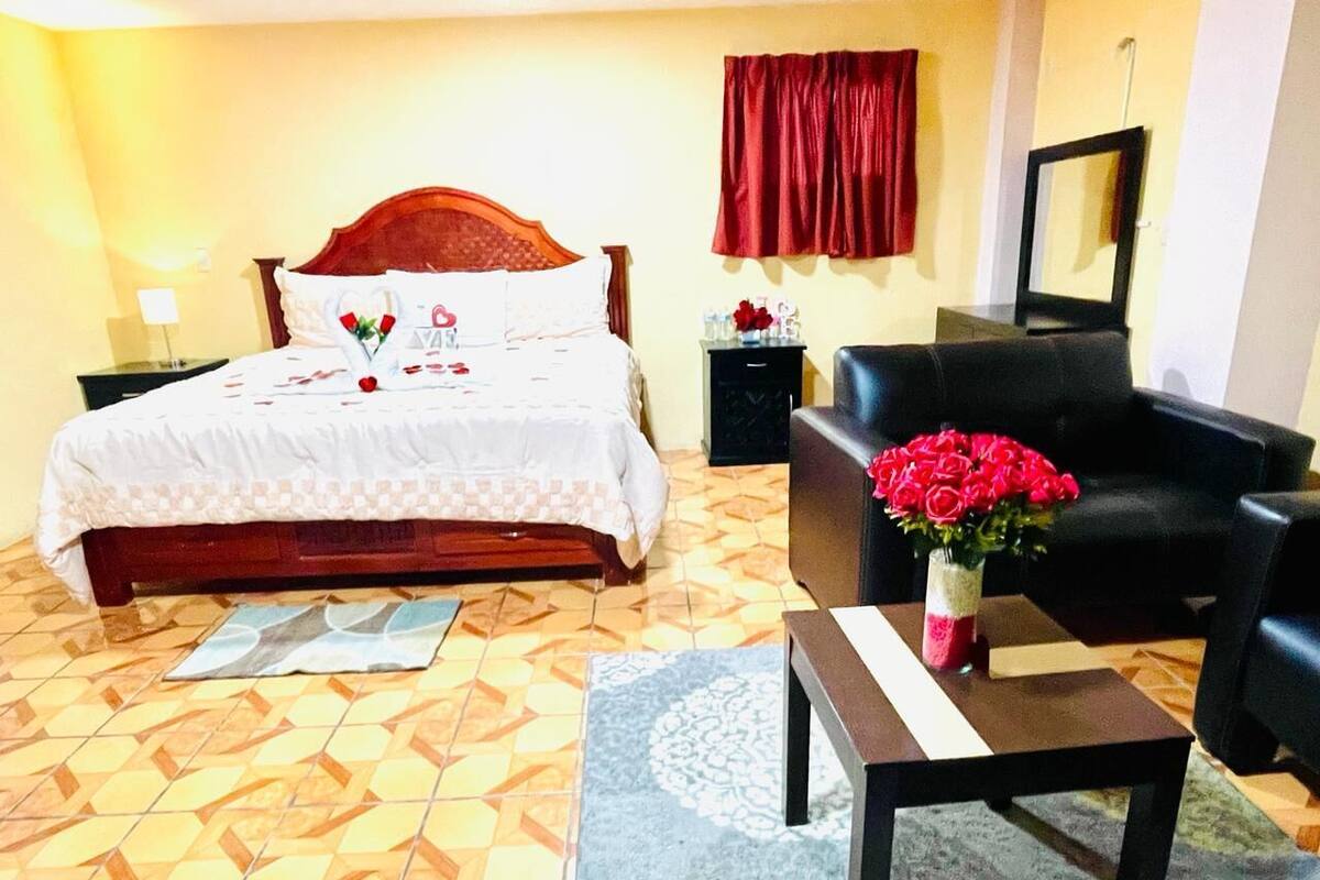 Une chambre d’hôtel avec un lit, une table de chevet, une chaise, une table et un vase avec des fleurs.