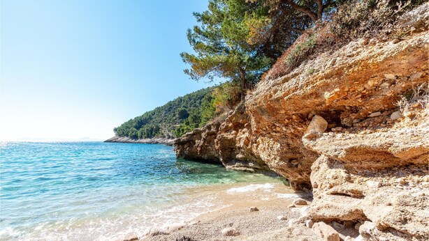 Una spiaggia costiera con acque cristalline blu, scogliere rocciose e vegetazione rada.