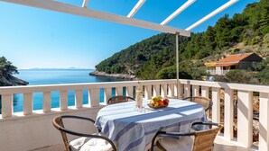 Un balcone con un tavolo apparecchiato per due, affacciato su una vista costiera, cielo sereno e una linea di costa in lontananza.