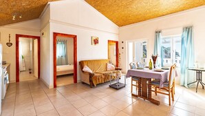 Un'ampia stanza con soffitto in legno, un divano, un tavolo da pranzo per quattro persone e vista sull'esterno attraverso ampie finestre.