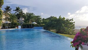 A swimming pool with a view of the ocean, surrounded by palm trees and a building with a balcony. - Premium 3-BR Ocean view Condominium at Hispaniola Beach! (Sosúa)