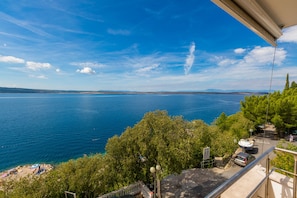 A balcony with a view of a large body of water, trees, and a distant shoreline. - Apartment Marko (Crikvenica)