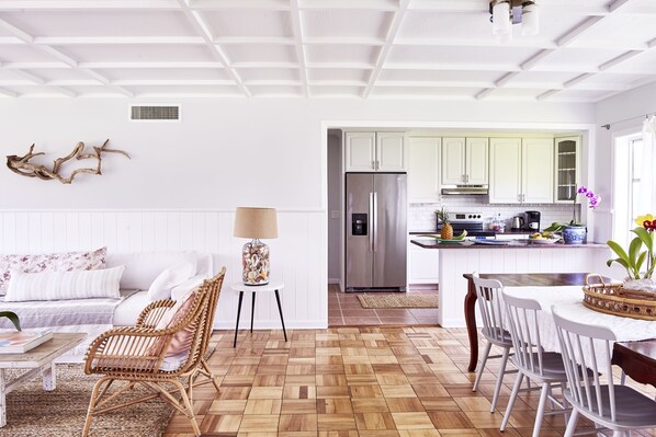 Une cuisine moderne avec des meubles blancs, un réfrigérateur en acier inoxydable et un coin repas comprenant des chaises et une table, le tout dans des tons de blanc.