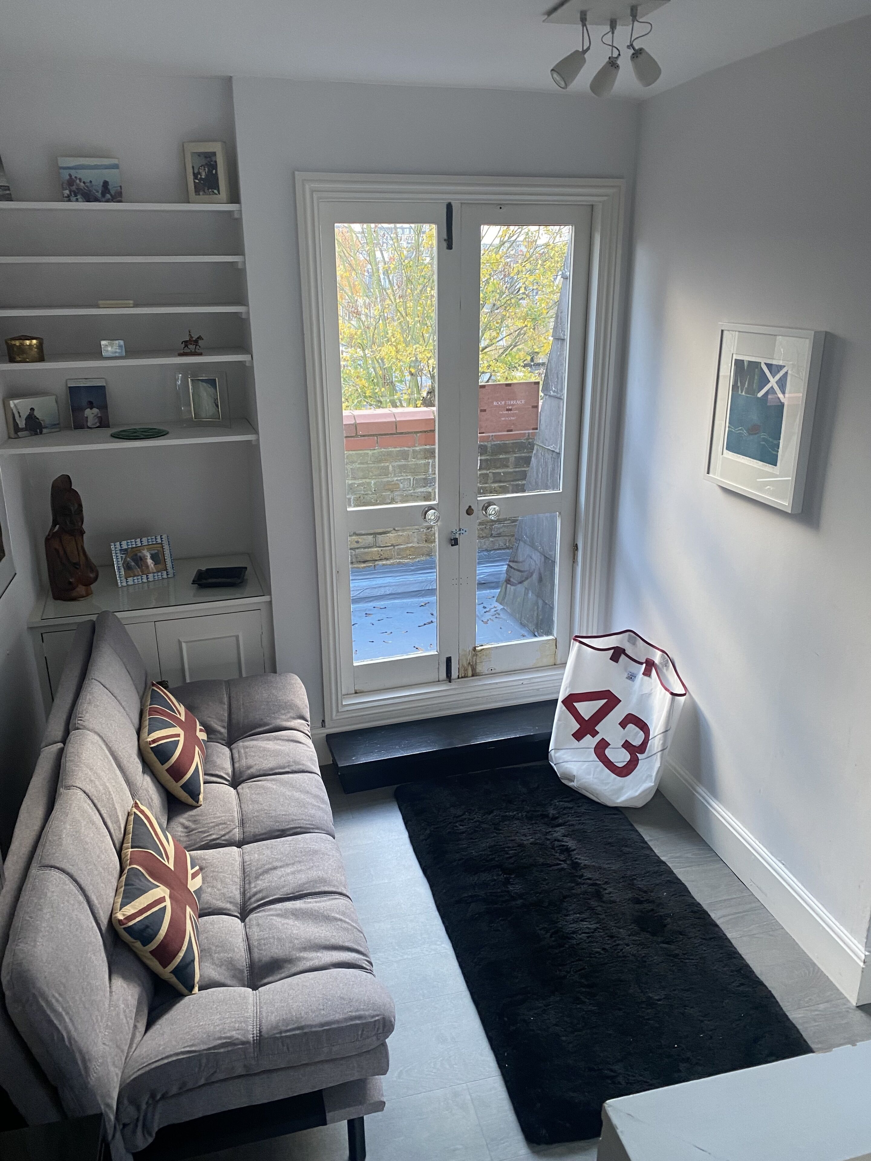 A living room with a grey sofa, black rug, and a white bag with the number 43.