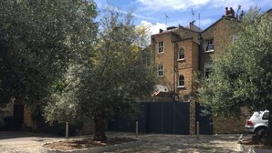 Ein gepflasterter Weg führt zu einem verschlossenen Eingang, im Hintergrund ein Backsteinhaus.