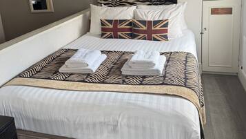 A neatly made bed with white linens and a patterned throw, a bedside cabinet, and a wall-mounted air conditioner.
