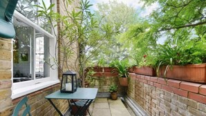 Eine kleine Terrasse mit Tisch und Stühlen, umgeben von einer Ziegelmauer und Kübelpflanzen.