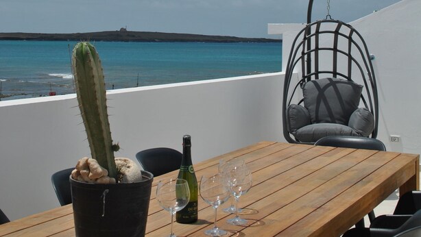 Una mesa de madera con un cactus en maceta, una botella de vino y copas en una terraza con vistas al mar.