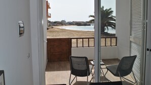 Un balcón con dos sillas y vista a la playa, con una palmera.