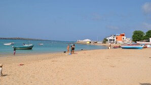 Una playa con barcos, gente y edificios al fondo.