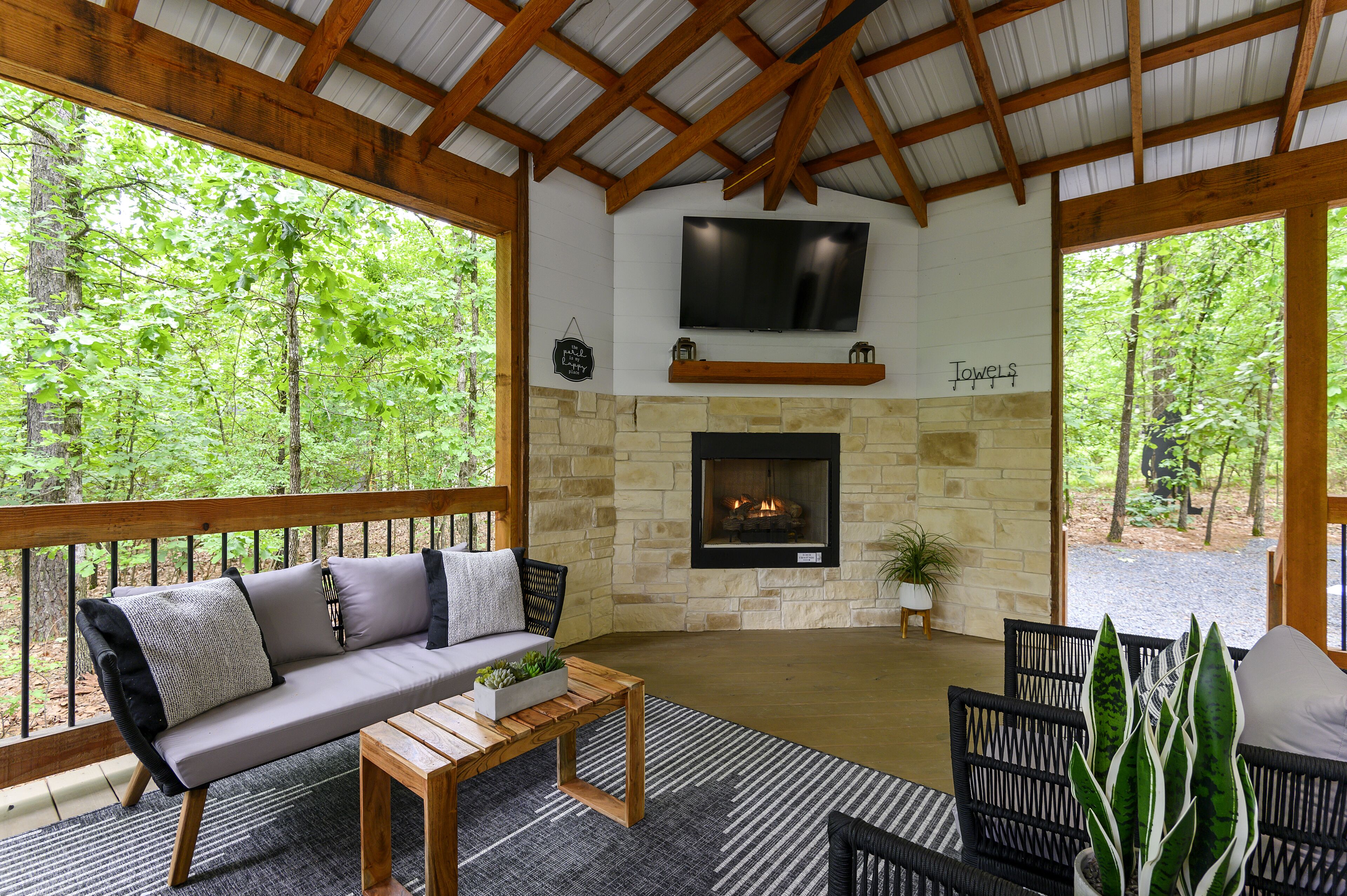 A cozy indoor seating area with a stone fireplace, a flat-screen TV, and a wooden ceiling.