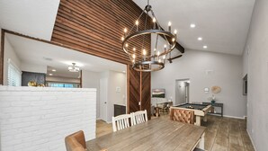 A spacious dining area with a wooden table and chairs, a pool table, and a modern chandelier. - Katy Home Fully Furnished King Beds 50" Televisions Pet Friendly 28+ Night Stays (Katy)