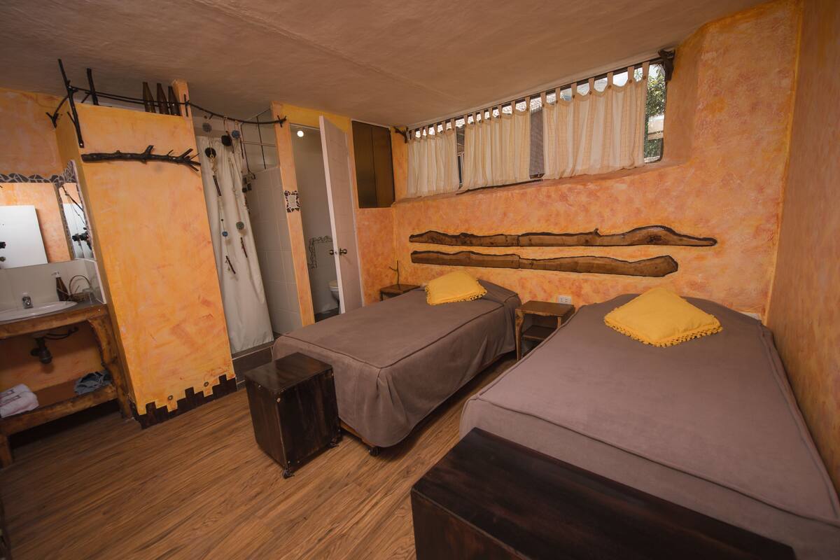 Una habitación con dos camas individuales, un banco de madera, una mesita y una ventana con cortinas.