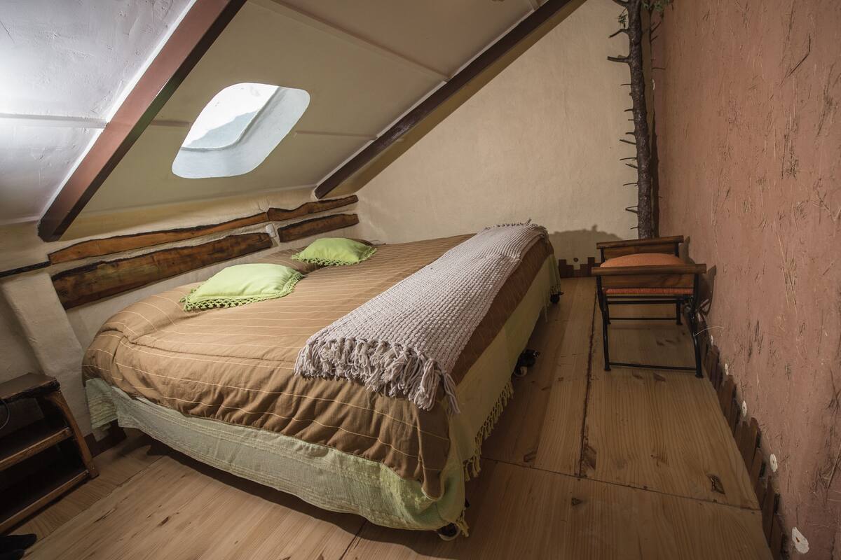 Un dormitorio acogedor en el ático, con techo inclinado, una cama individual, una silla y un tragaluz.