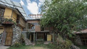 A two-story house with a stone facade, a wooden door, and a balcony with metal railings. - Eco Tampu - Andahuaylillas (Andahuaylillas)