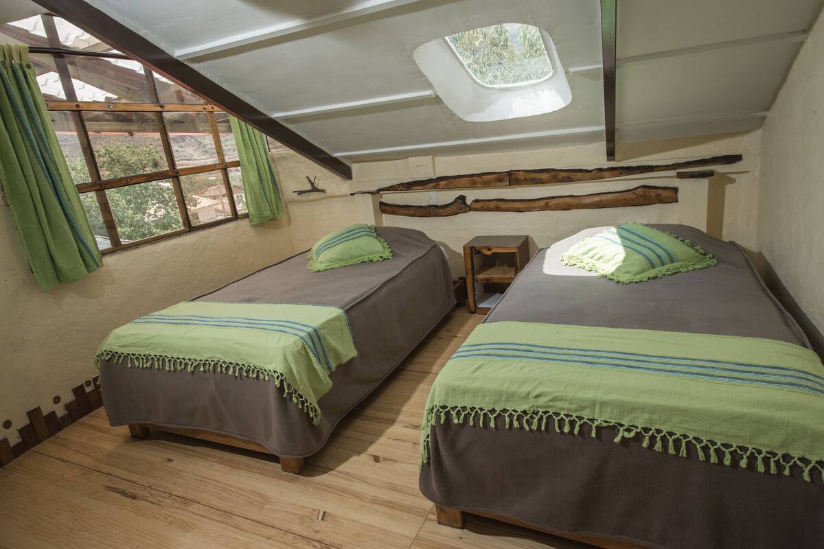 Una habitación con dos camas, un tragaluz y una ventana con cortinas.