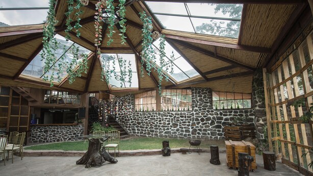 A spacious interior with a stone wall, wooden furniture, and hanging plants. - Eco Tampu - Andahuaylillas (Andahuaylillas)