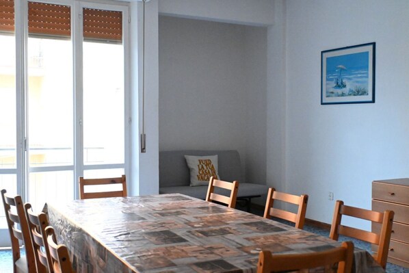 A dining area with a table, chairs, a sofa, and a wall-mounted picture.