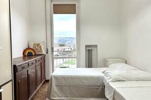 A bedroom with a bed, a dresser, a radiator, and a window with a view of a town.