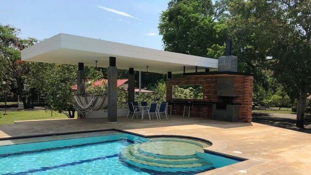 Una piscina amb una zona circular submergida, una zona de seients coberta i una estructura de maó amb una xemeneia.