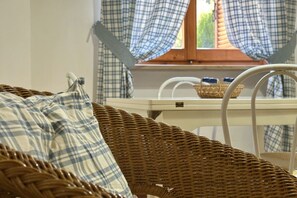 A wicker chair with a plaid cushion, a wicker basket, and a white chair with a blue cushion.