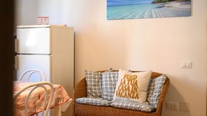 A room with a wicker sofa, a white refrigerator, and a wall-mounted painting of a beach scene. - N040 - Numana, three-room apartment a stone's throw from the center (Numana)