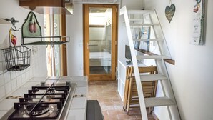 A narrow kitchen with a gas stove, a wooden door leading to a bedroom, and a white shelf with a heart-shaped decoration. - M225 - Marcelli, new one bedroom apartment with garden (Marcelli)