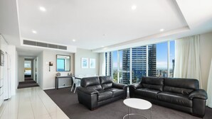 A modern living room with two black leather sofas, a white coffee table, and a large window offering a city view.