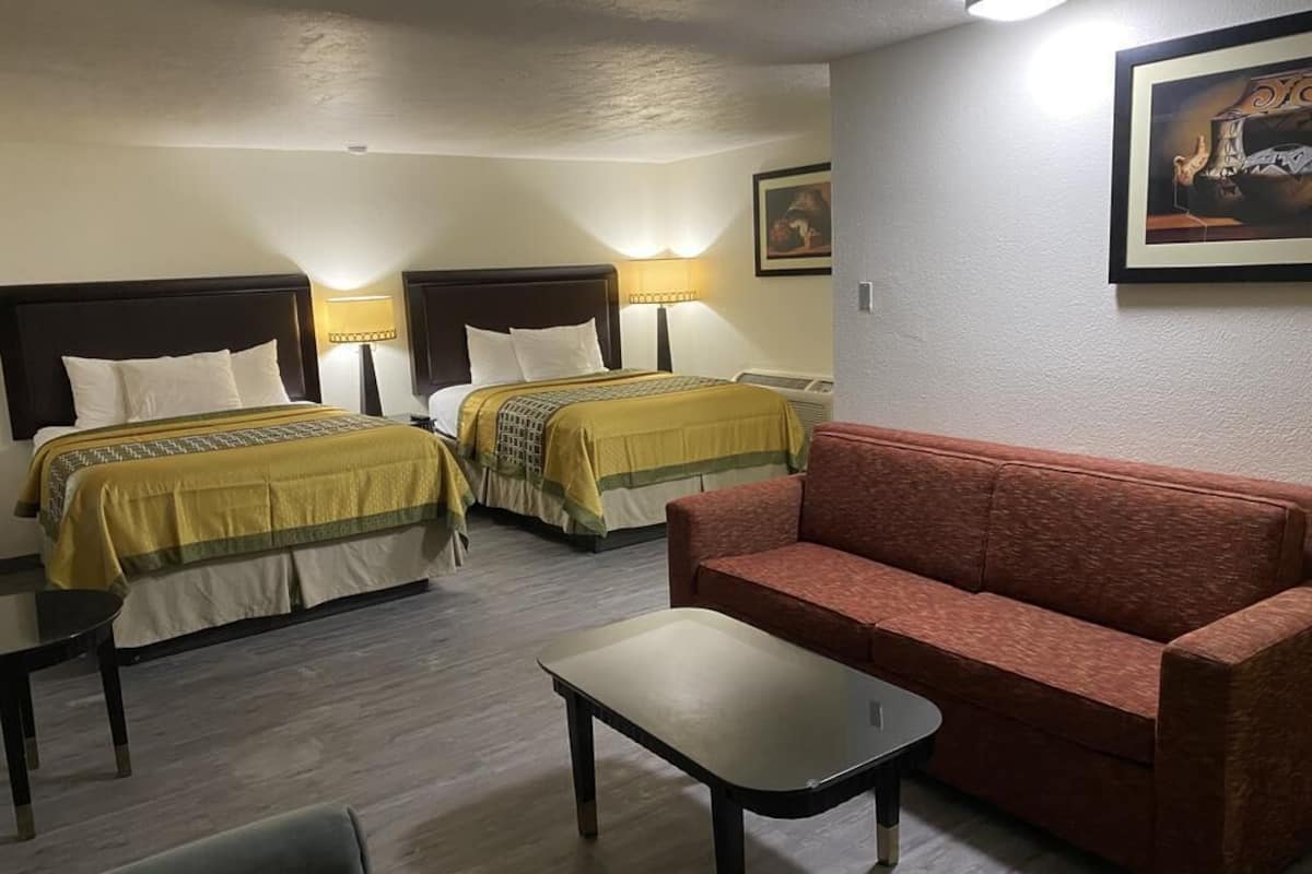 A hotel room with two beds, a red sofa, a small table, and a painting on the wall.