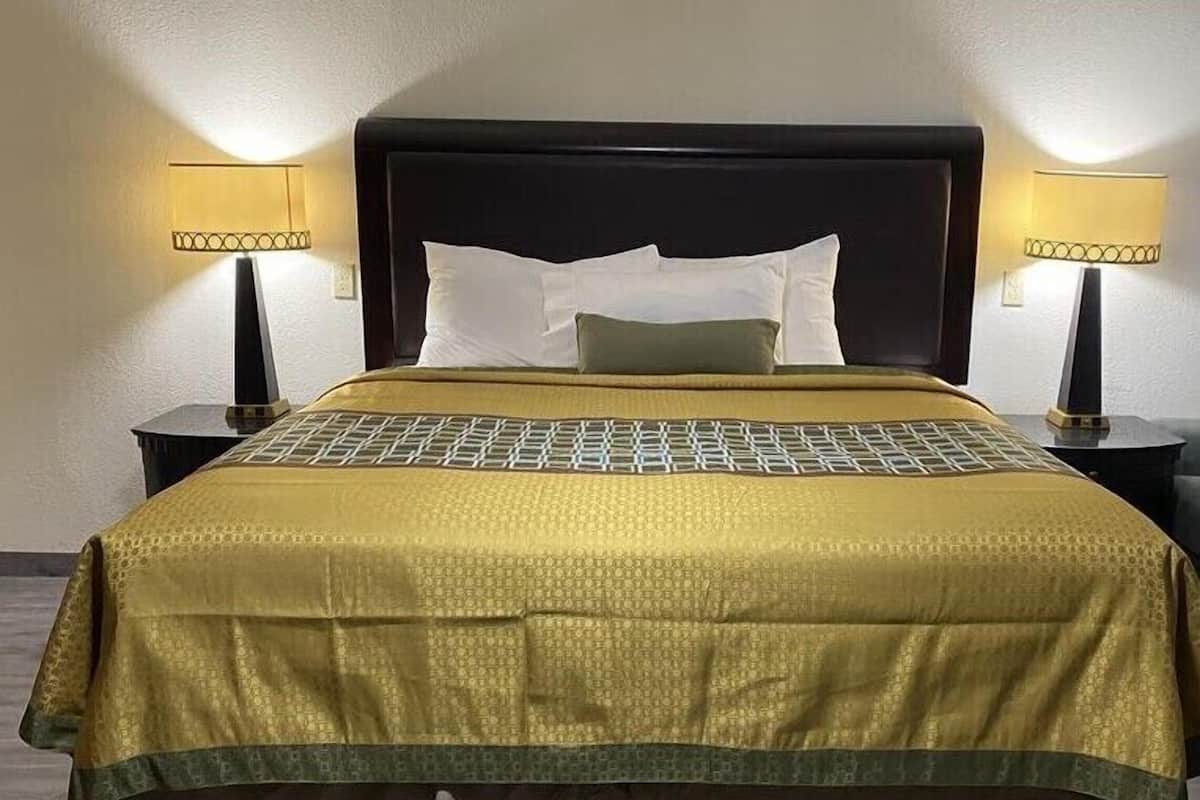A neatly made bed with a patterned bedspread and pillows, flanked by two bedside tables with lamps, set against a plain wall.