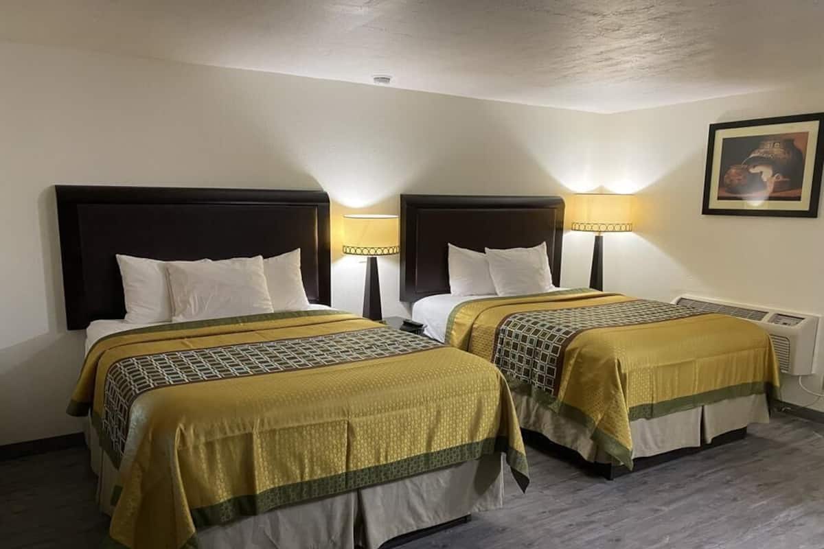 A hotel room with two beds, each with a headboard, bedside lamps, and a framed picture on the wall.