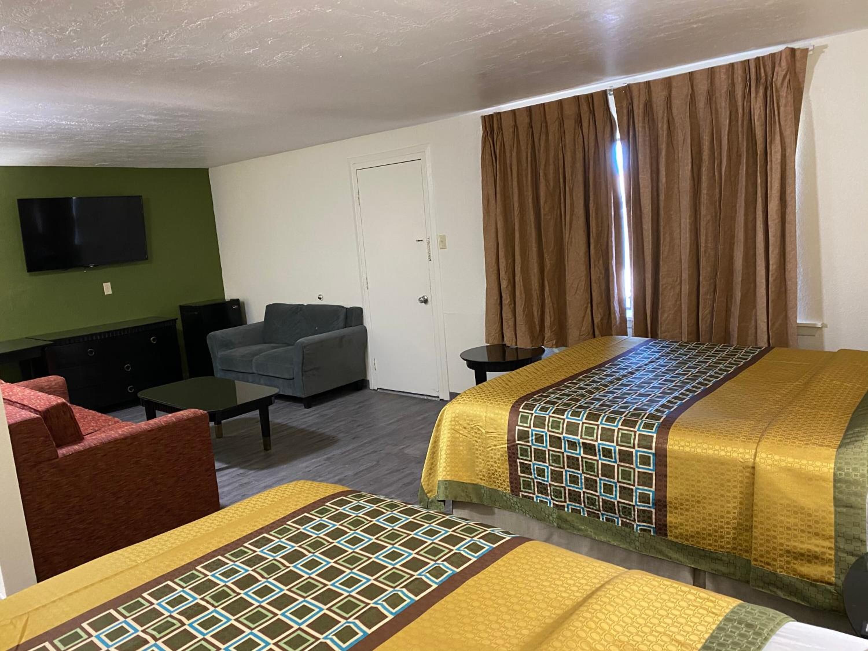 A hotel room with two beds, a TV, a sofa, and a small table.
