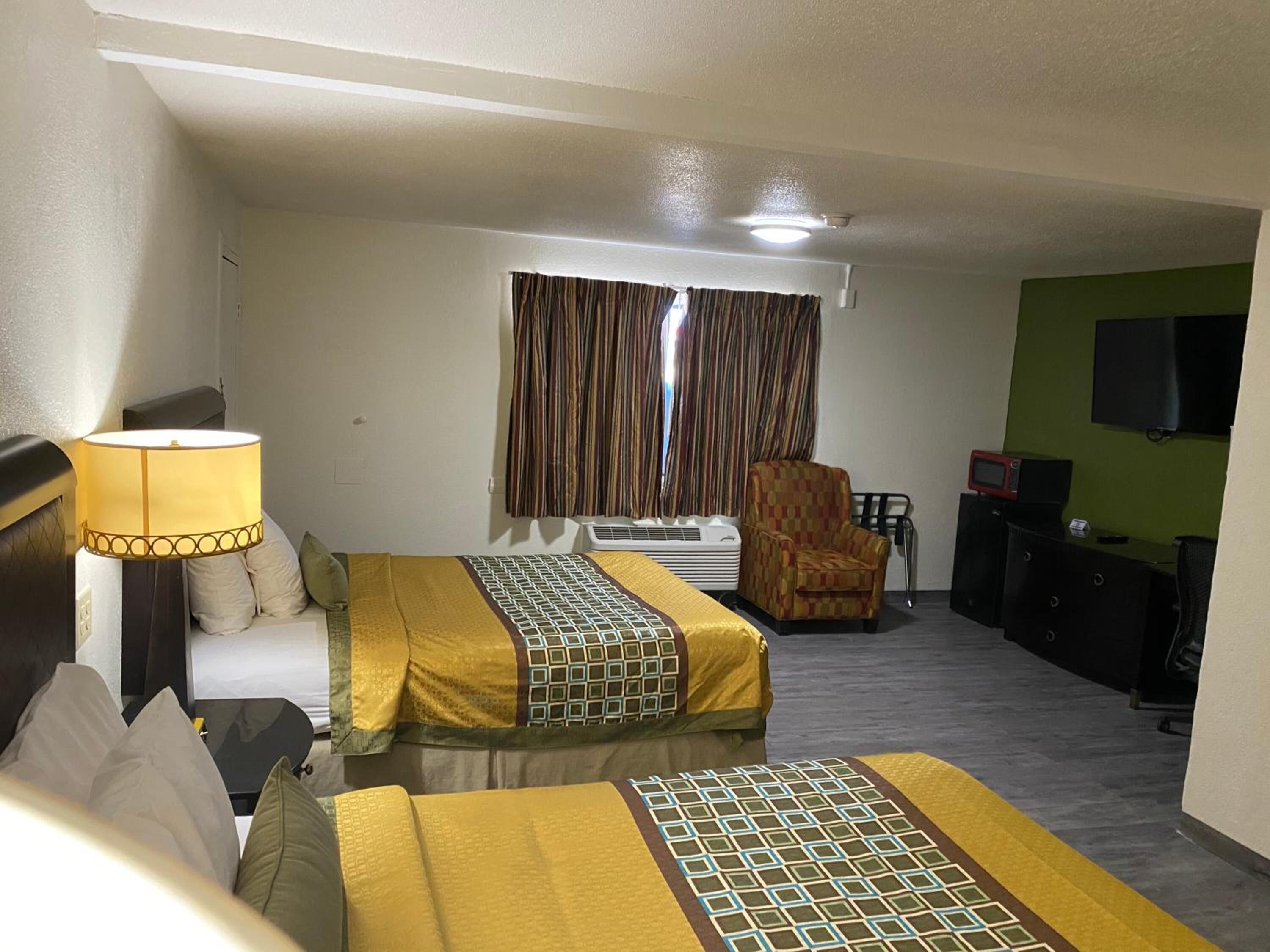 Une chambre d’hôtel avec deux lits, un bureau, une chaise, une télévision et une fenêtre avec des rideaux.