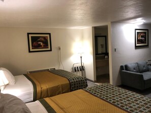 Habitación de hotel con dos camas, un escritorio, una silla y un baño visible a través de una puerta abierta.