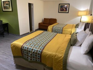 Habitación de hotel con dos camas, un sofá marrón, un escritorio y una silla.
