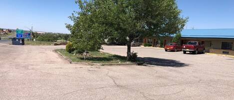 A parking lot with a large tree, a building with a blue roof, and a few parked cars.