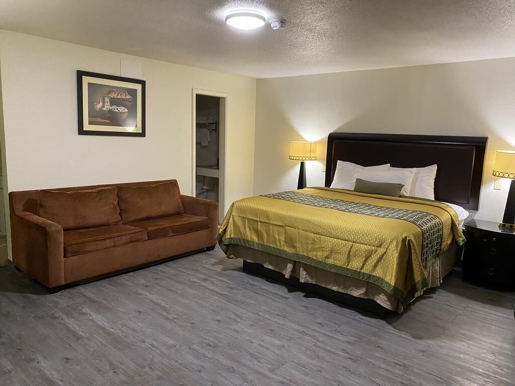 Une chambre d’hôtel avec un lit, un canapé marron et un tableau encadré au mur.