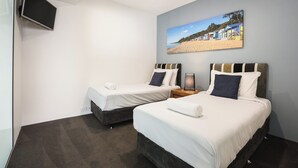 A hotel room with two beds, a flat-screen TV mounted on the wall, and a beach scene painting above the beds.