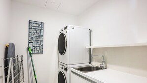 A laundry room with a stacked washer and dryer, a sink, and a blue mop bucket.