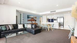 A modern living room with a black leather sofa, a glass coffee table, and a dining area with a white island and chairs.