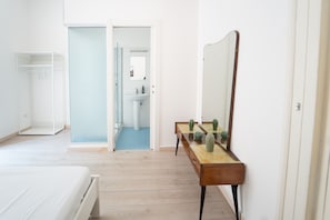 A bedroom with a bed, a wooden dresser, a mirror, and a bathroom visible through an open door.