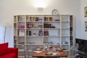 A living room with a bookshelf, a dining table with clear chairs, a red sofa, and a television.