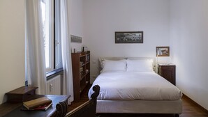 A bedroom with a bed, a wooden nightstand, a bookshelf, and a window with curtains. - Cozy Family Apt in Castelletto by Wonderful Italy (Genova)