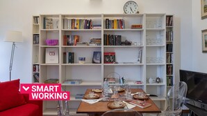 A smart working space with a bookshelf, a dining table with clear chairs, and a television. - Cozy Family Apt in Castelletto by Wonderful Italy (Genova)