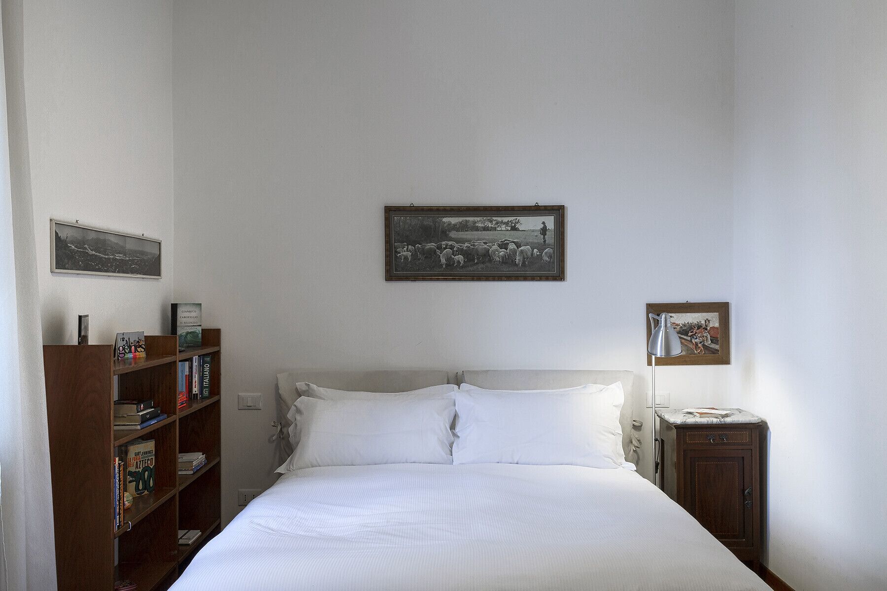 A bedroom with a bed, a bookshelf, and two framed pictures on the wall.