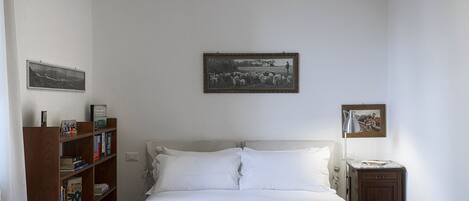 A bedroom with a bed, a bookshelf, and two framed pictures on the wall.